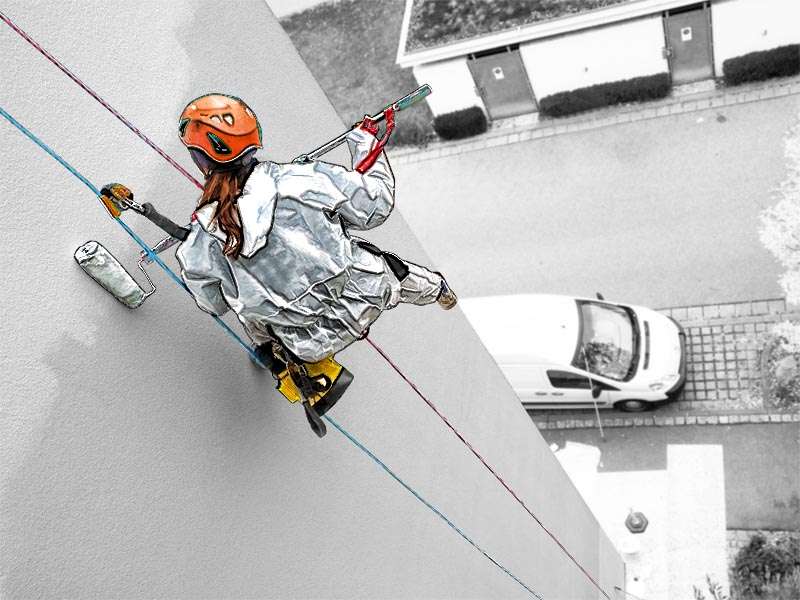 Ausgebildeter Höhenarbeiter bei Malerarbeiten an einer Hauswand